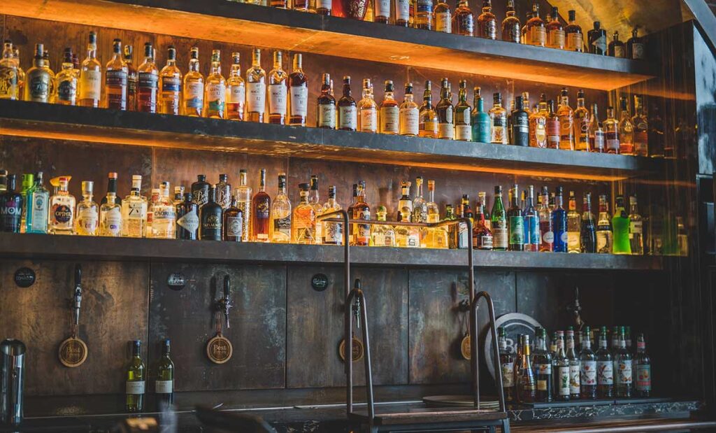 A wooden wall with shelves full of alcohol. 