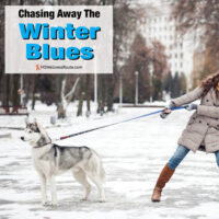 Woman holding back husky in the snow with overlay: Chasing Away The Winter Blues