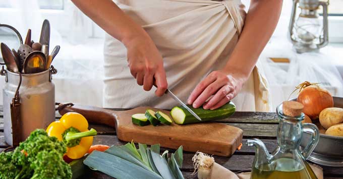 Woman cutting up vegetables on a cutting board.
