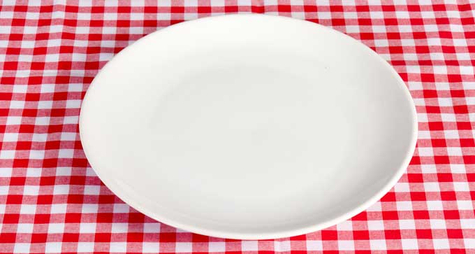 A white empty plate on a red and white checkered tablecloth.
