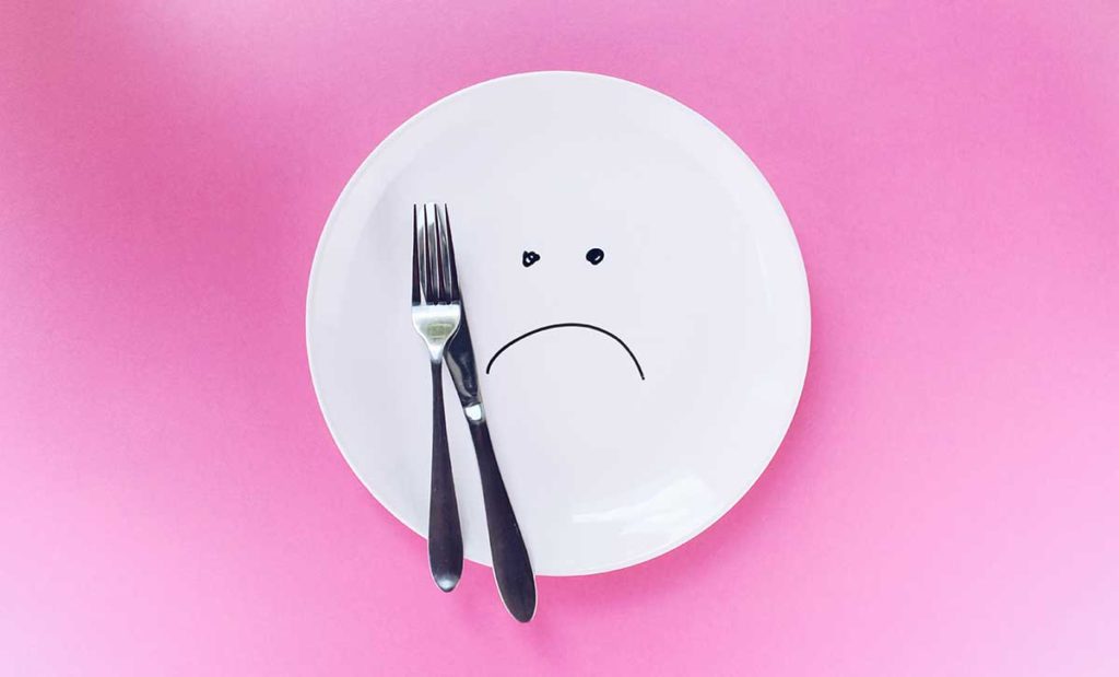 Empty white plate with a drawing of a frowning face on pink background.