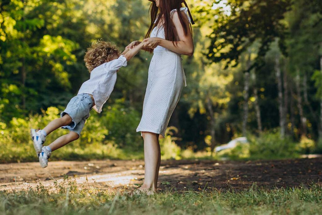 Mother swinging son by his arms in the park.