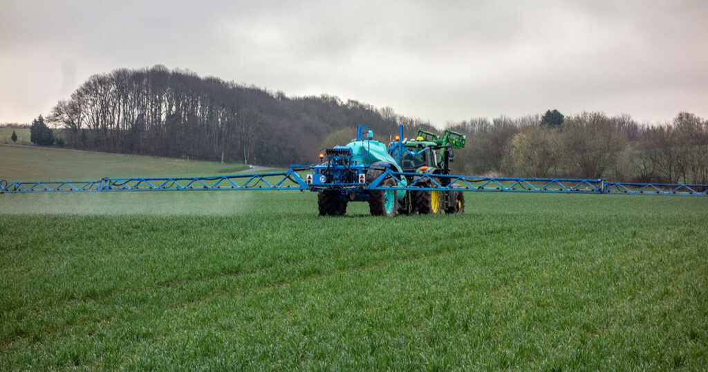 Tractor spraying pesticides on farm field.