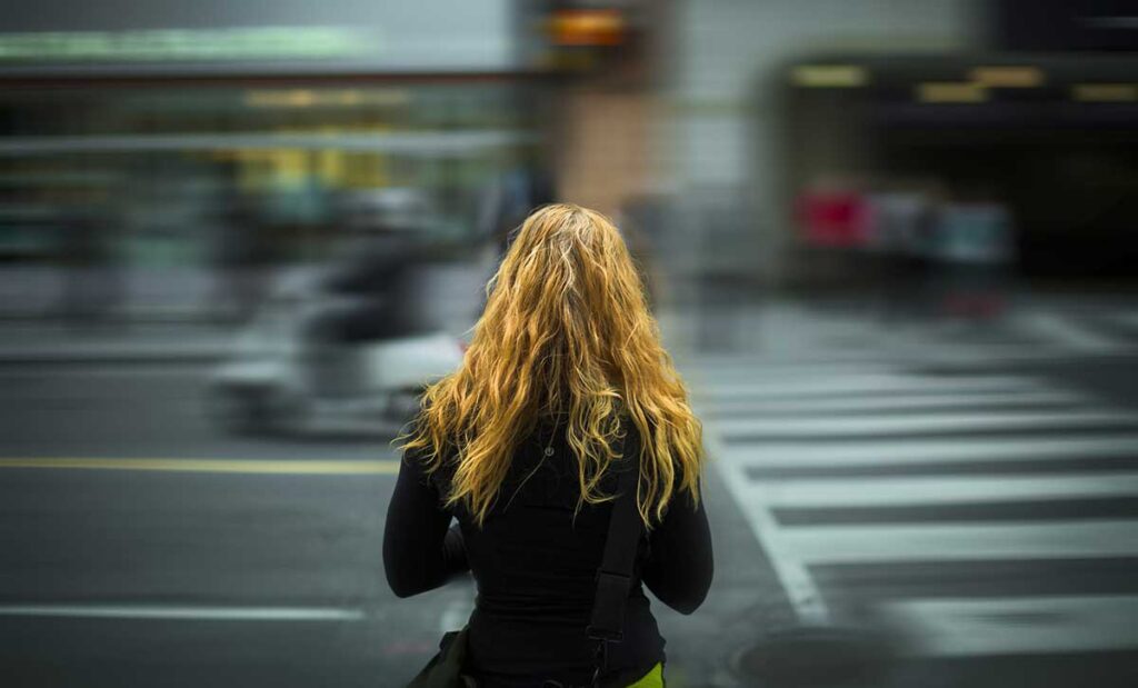 Traffic rushing past woman with long hair.