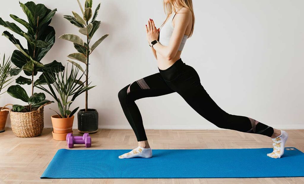 Slender woman standing in Crescent Lunge yoga position with Prayer Hands.