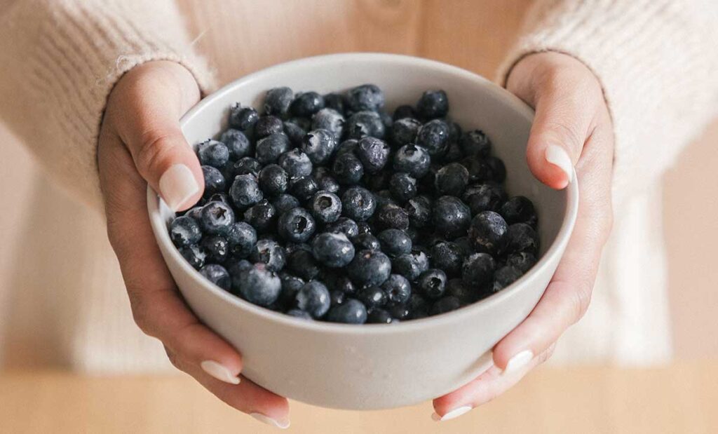 Woman holding a bowl of blueberries.