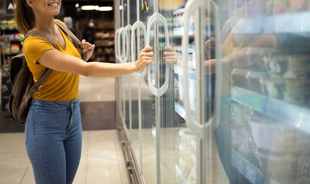 Young woman shopping the freezer section at a grocery store.