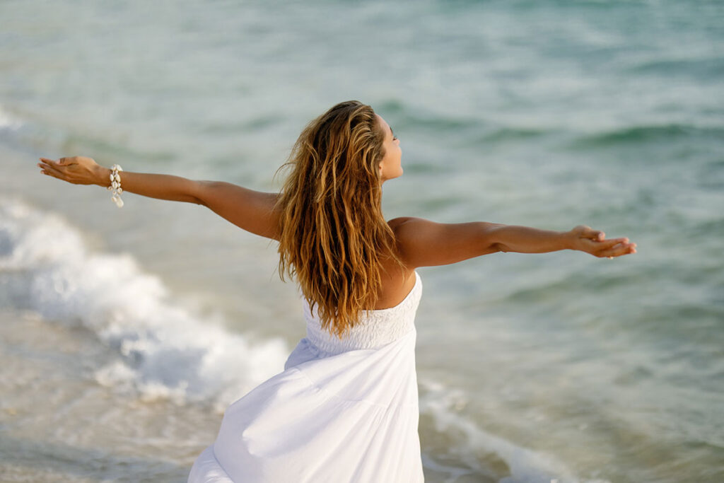 Back view woman feeling free while standing by sea with her arms outstretched to her sides.