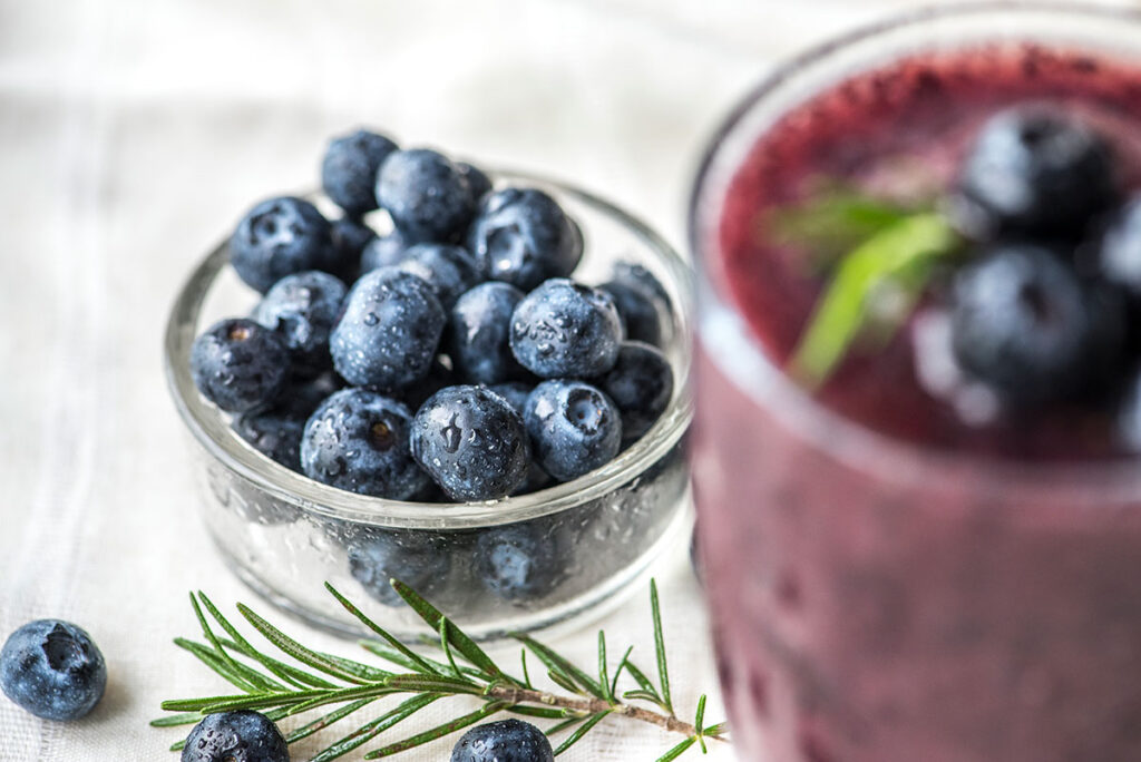 Close up of wild blueberries in a glass dish with a blueberry smoothie.