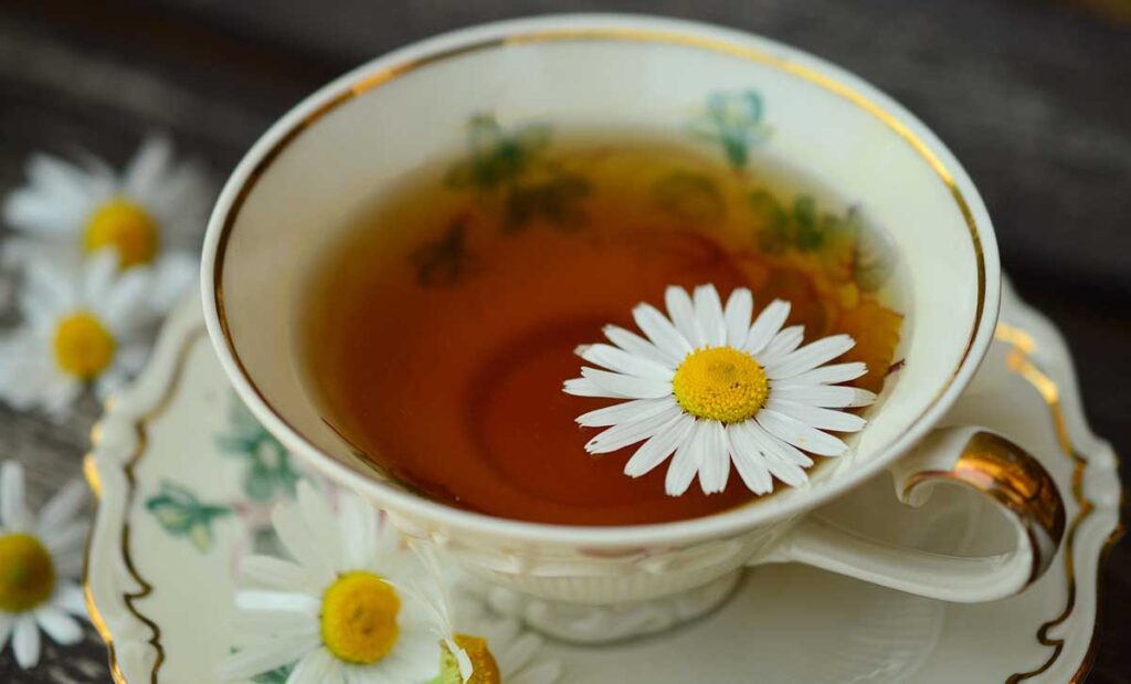 Chamomile tea in a teacup with a chamomile flower on top.