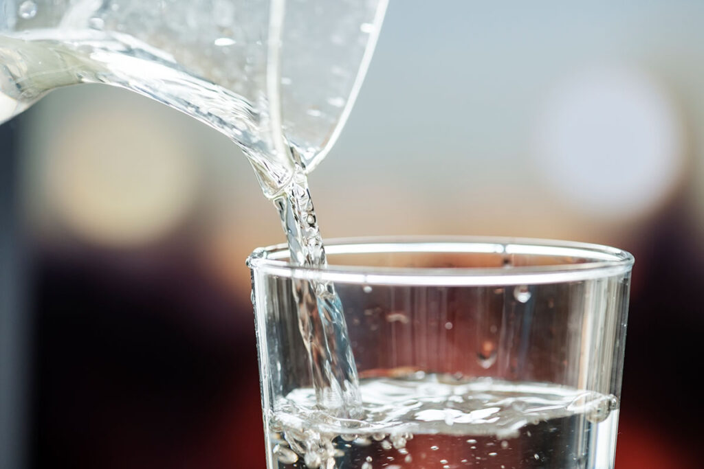 Close up image of glass container pouring water into glass.