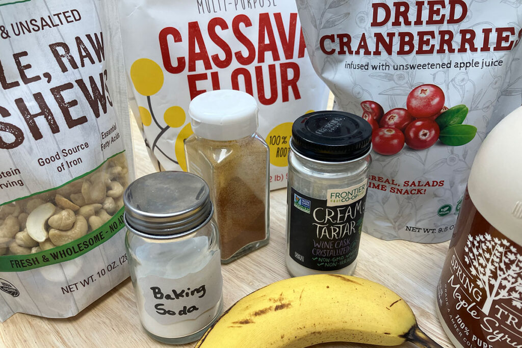 Packages of cashews, cassava flour, dried cranberries, maple syrup, seasoning, and a banana.