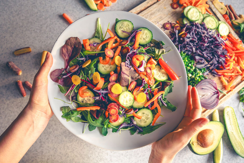 Female hands holding a bowl of vegan salad with fresh vegetables top view.