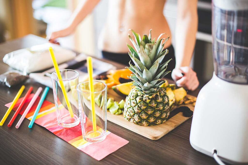 Fitness girl preparing two smoothies with pineapple.