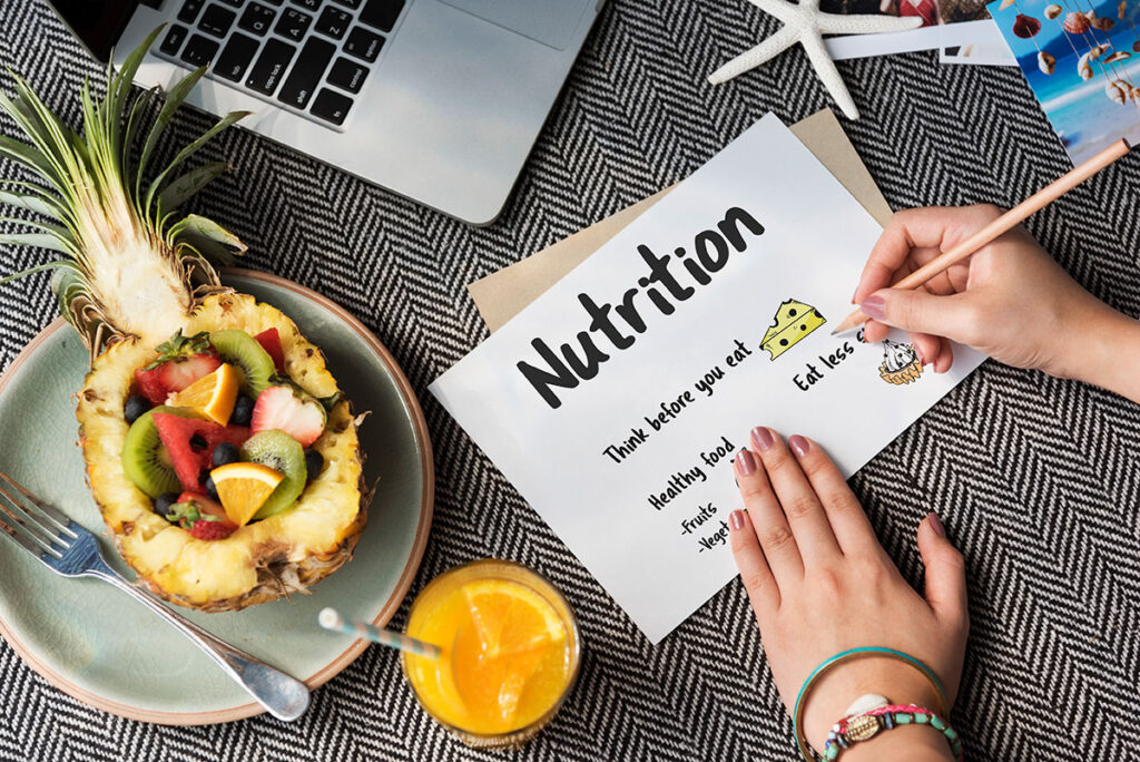 Woman writing nutrition list with pineapple cored out and filled with fruit.