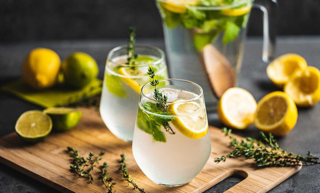Two glasses of water with lemon slices and herbs.