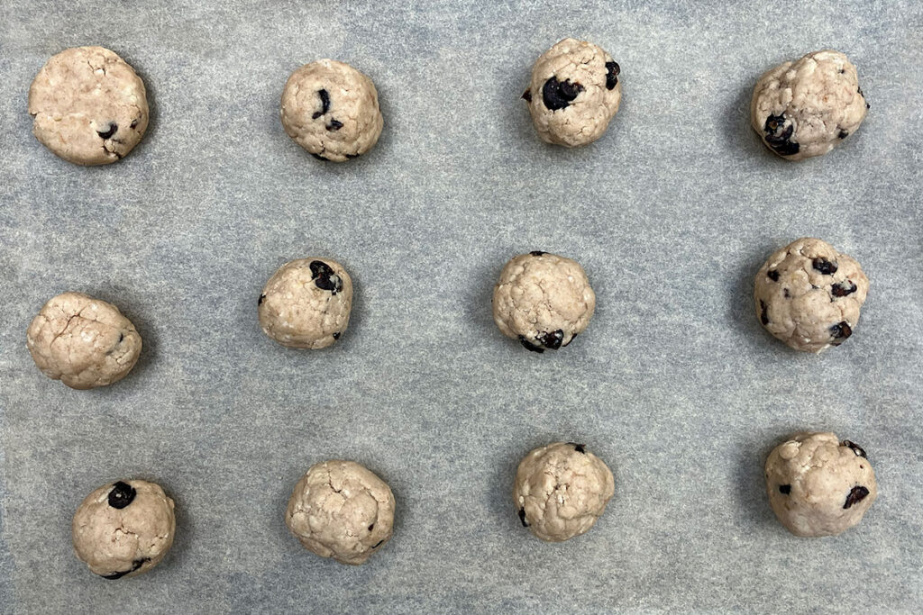 Raw cranberry cookie dough rolled into balls on parchment paper.