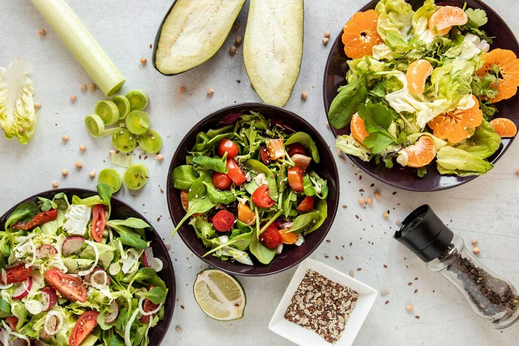 Salads in bowls with fruits and vegetables on white table.