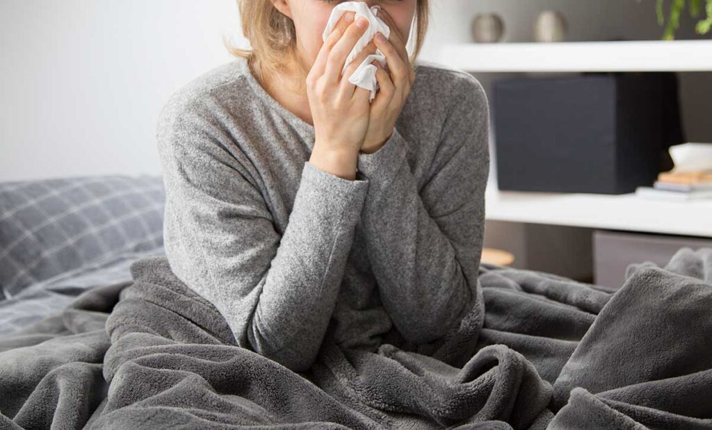 Sick woman sitting up in bed blowing her nose.