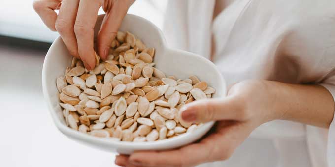 A woman eating pumpkin seeds from a heart shaped bowl.