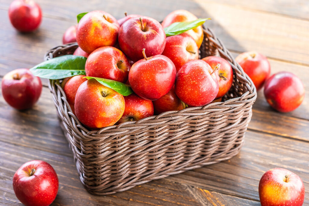 Red apples in a wicker basket on a wood table.