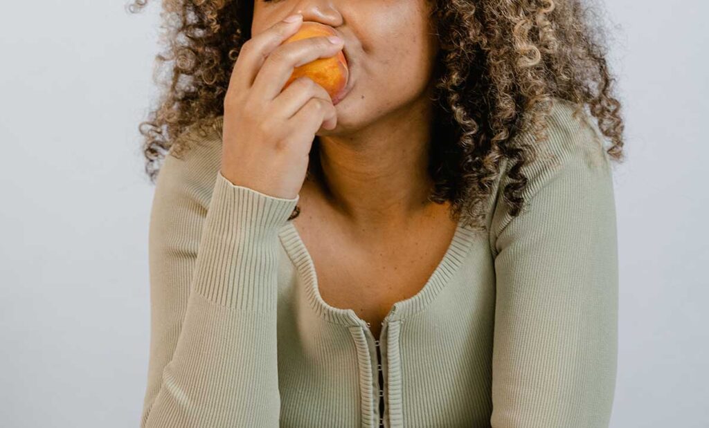 Woman Wearing Long Sleeve Shirt Eating a Fruit