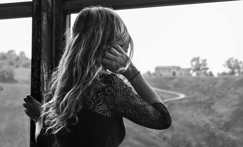 Black and white photo of a young woman looking out the window.