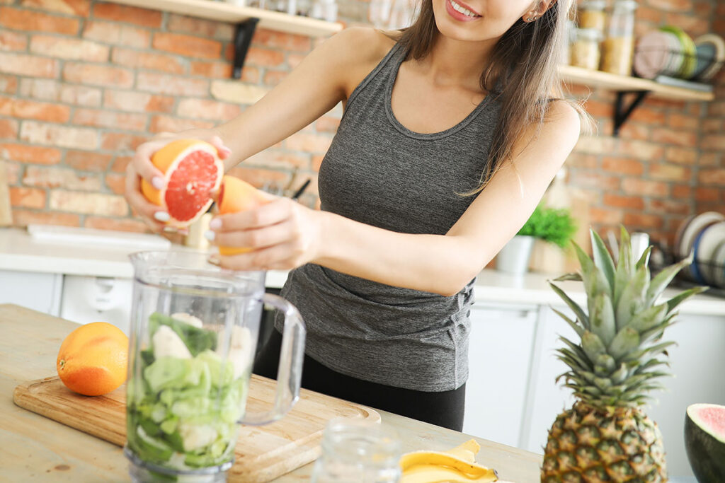Young woman squeezing an orange into a smoothie pitcher.