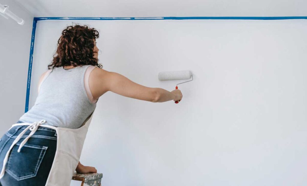 Woman standing on a ladder painting the wall white,