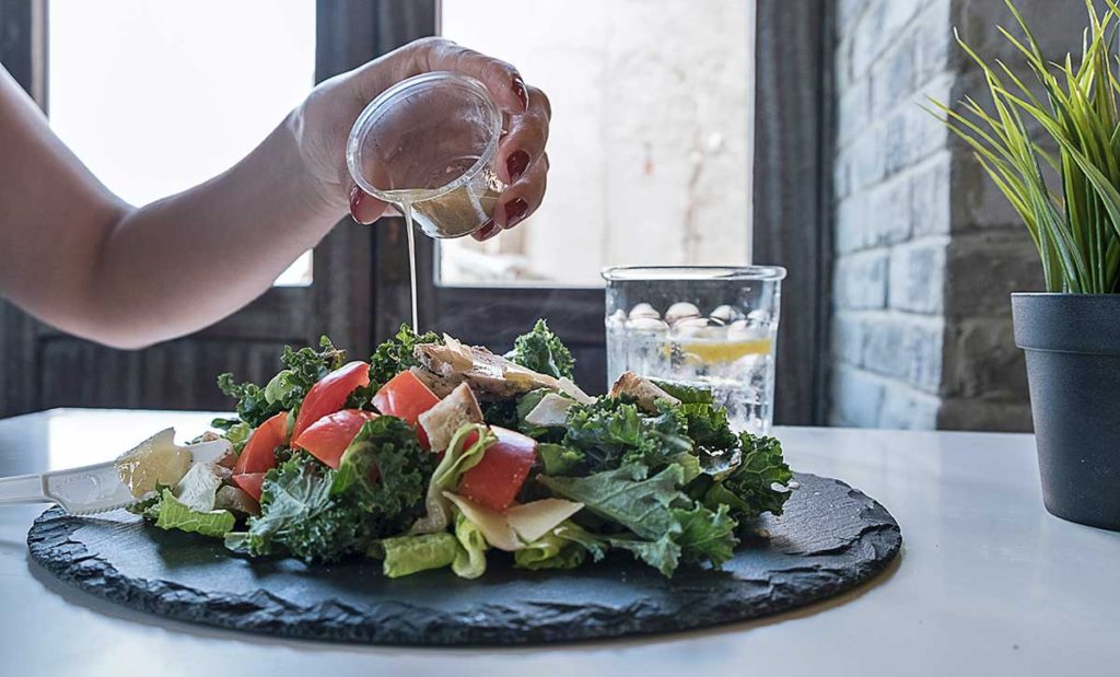 Woman pouring dressing on salad.