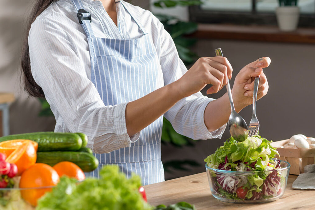 Woman in blue and white stripped apron preparing a salad.