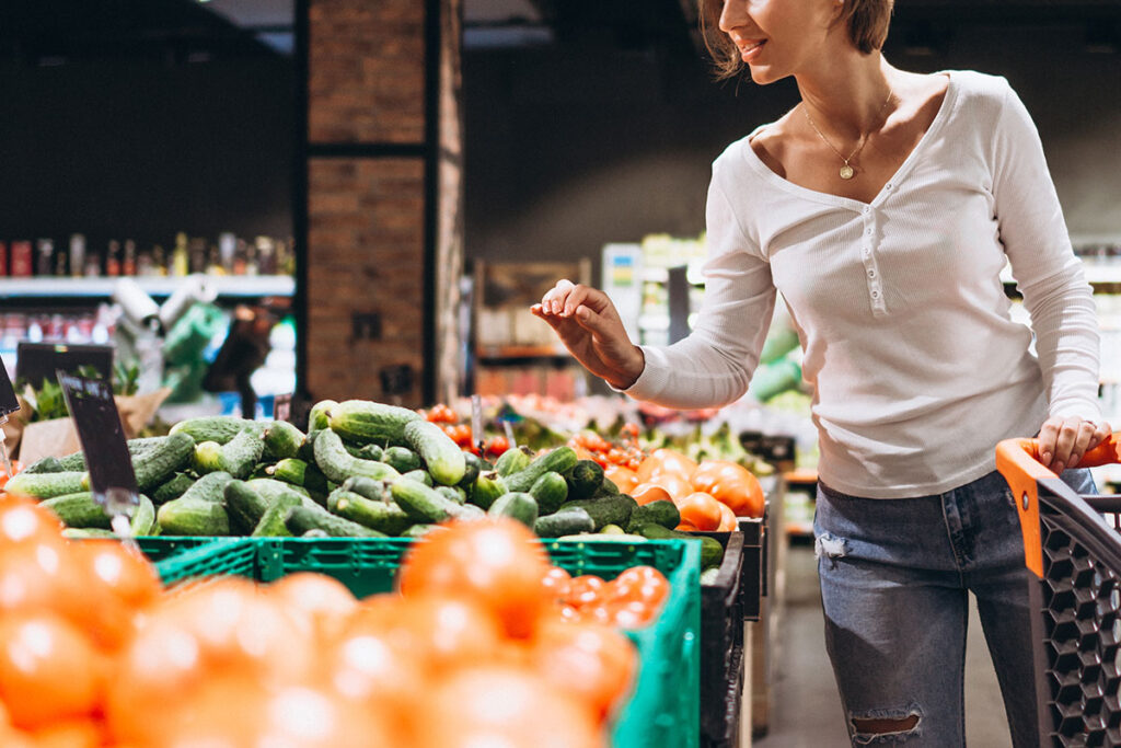 Blond woman in white top and jeans shopping for produce.
