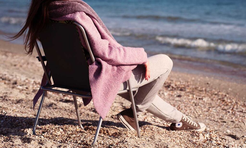 Woman sitting in a chair on a beach looking at the ocean.