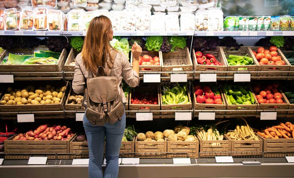 woman standing front vegetable shelves choosing what buy.