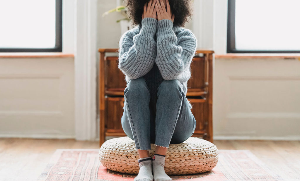 Stressed woman sitting on pillow covering face.