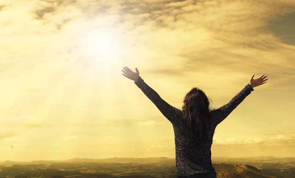 Woman in sunlight with open arms.