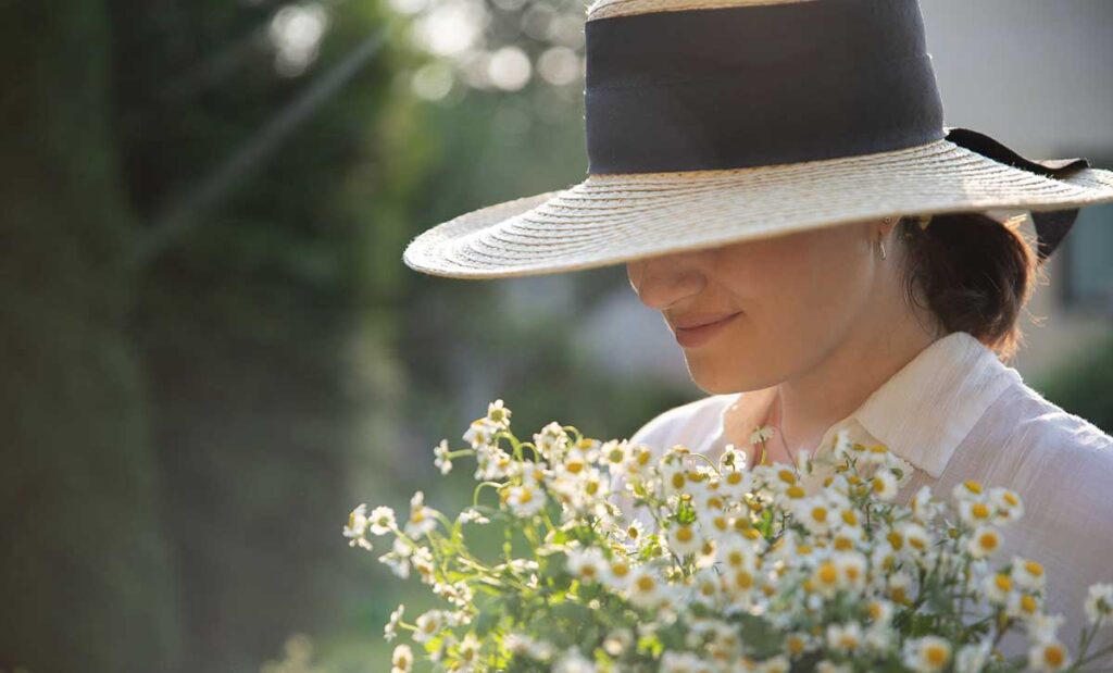 Young woman wearing a hat holding flowers.