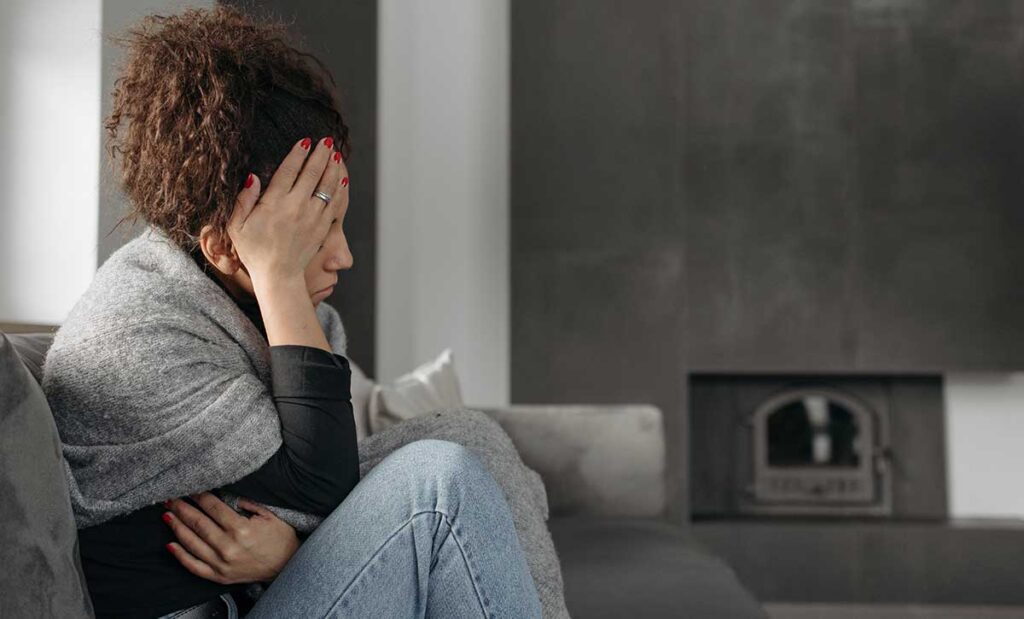 Woman with headache holding her head sitting on a sofa.