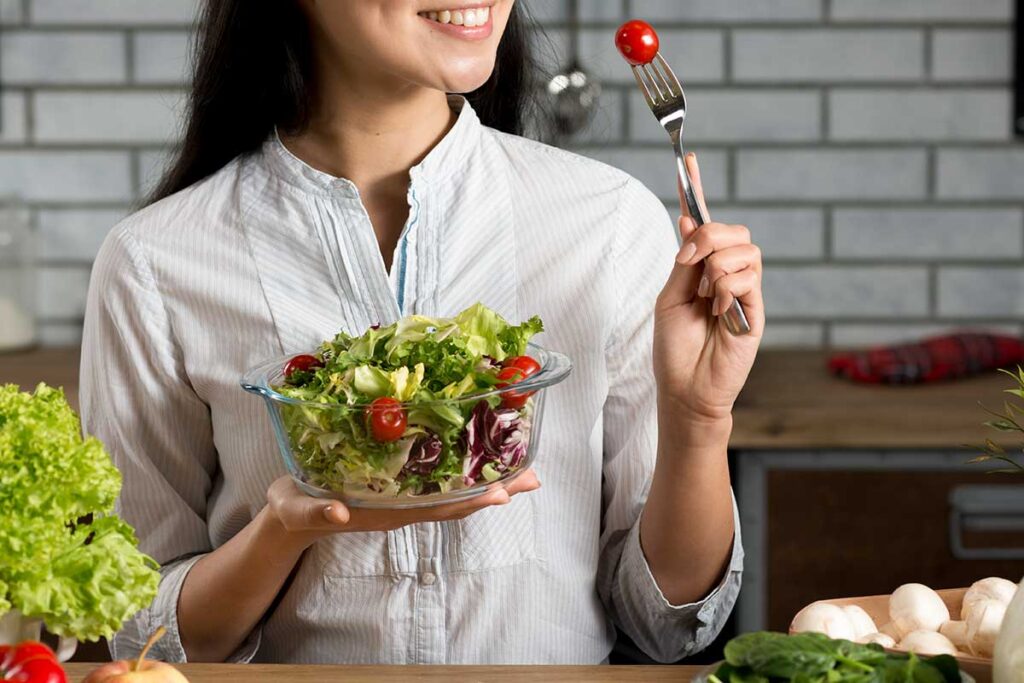 Woman holding and eating a healthy salad in the kitchen.