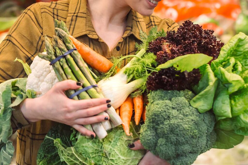 Close up of young woman grocery shopping with an armful of vegetables.